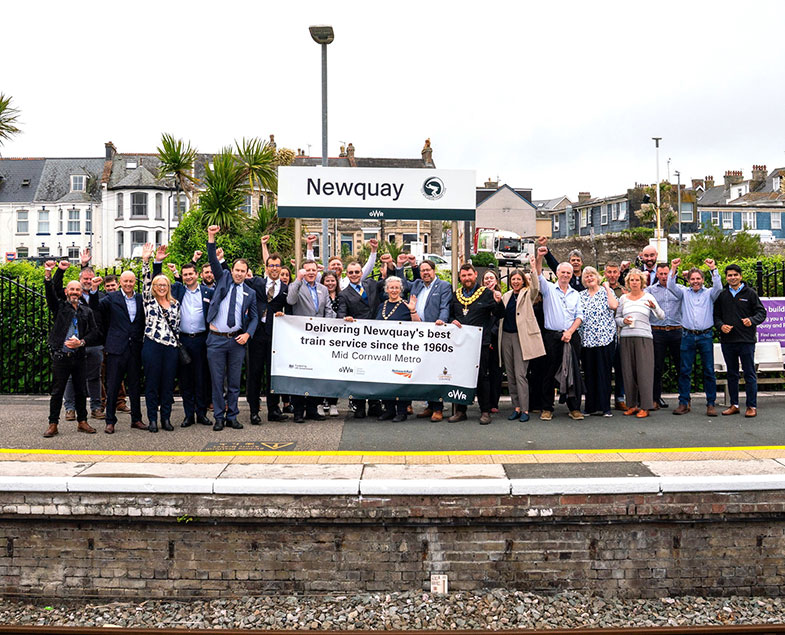 Stakeholders on platform in front of Newquay station sign celebrating the town's new hourly train service